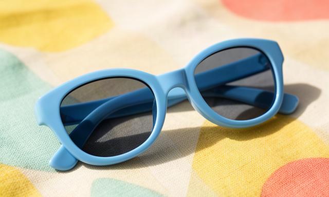 Kinder-Sonnenbrille mit blauem Gestell auf einer bunten Picknickdecke